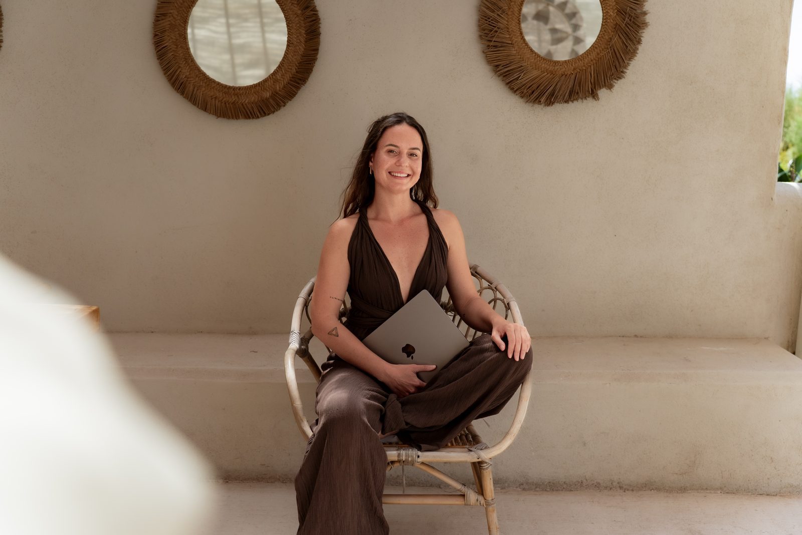 Uli, embodied living coach, working on laptop in a rattan chair